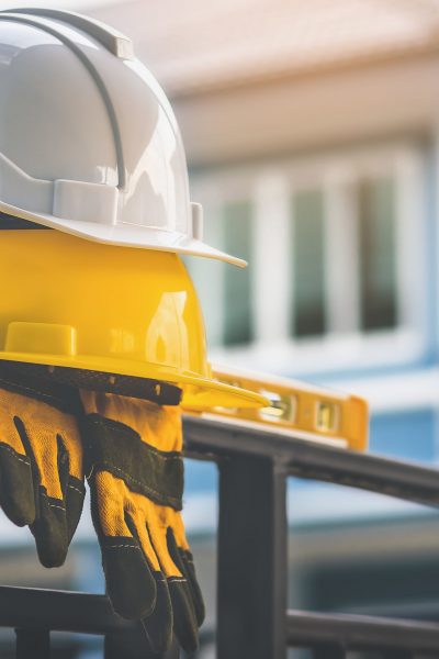White and yellow helmet  with gloves are placed on steel house fence.